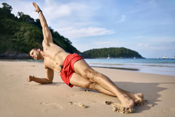 Sportive guy training on beach. Daylight shooting.