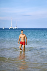 Tanned guy in red shorts on beach. Daylight shooting.