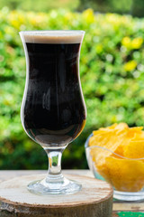 A glass of cold dark beer on wooden table in the garden - closeup with selective focus