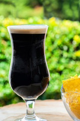 A glass of cold dark beer on wooden table in the garden - closeup with selective focus