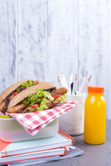 A sandwich with sausages and salad in a lunch box with vegetables and fresh juice in a bottle. Delicious and healthy lunch for school and office. Lunch for two,