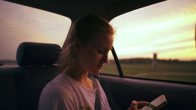 Young girl texts while sitting in back seat of car at dusk