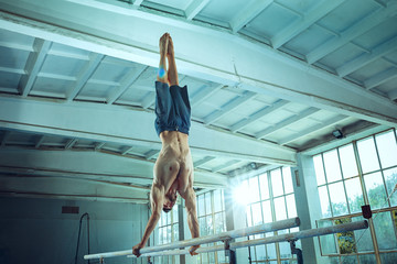 The sportsman performing difficult gymnastic exercise at gym. The sport, exercise, gymnast, health, training, athlete concept. Caucasian fit model