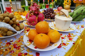 Top view of holy worship with Orange, banana, coconut, Dragon fruit, grape, flowers and colorful water to worship on the table, Religion concept
