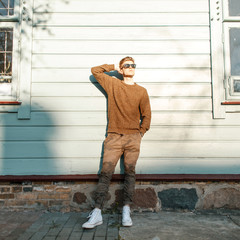 Handsome young guy in a stylish pullover with military pants and white shoes posing near the...