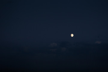 three-quarters of the growing moon in the navy blue sky with some visible clouds
