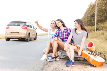 three young beautiful European-style girls friends hitch-hiked. A women with a chedoman on the road waiting for a passing car