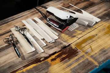 Combs, scissors and hair clipper on painted wooden table in barber shop