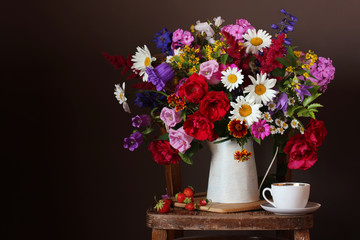 Bouquet of cultivated flowers in a jug on a chair and strawberries.