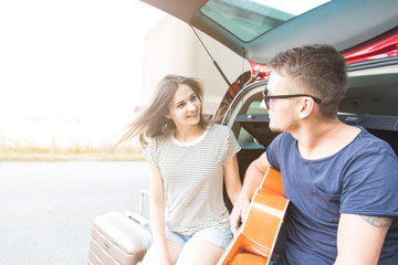 Yound Couple with suitcases on a trip by car. They sit in the back of the car, they look at the map, resting after a long drive and having fun. Hitchhiking and car trips with loved one