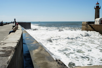 People relaxing on the quay in Foz do Douro, near Porto, Portugal, with Felgueiras Lighthouse on the side.