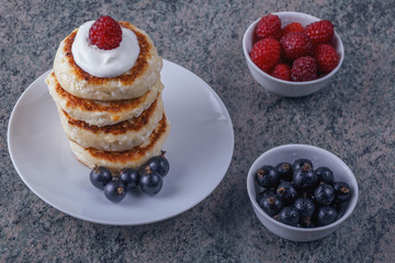 a pile of pancakes with cream and fresh berries on a wooden background.