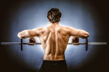 Muscular man doing shoulders exercise with barbell