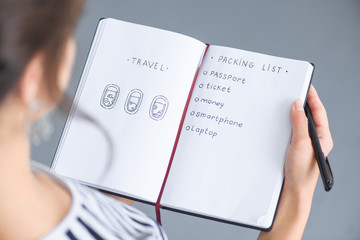 partial view of woman with pen holding notebook with packing list for traveling