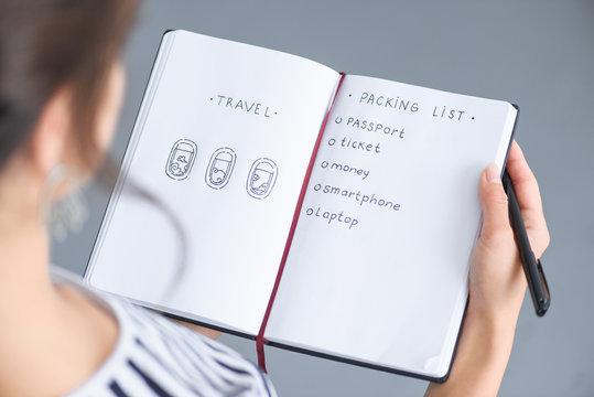 partial view of woman with pen holding notebook with packing list for traveling