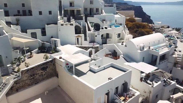 A beautiful woman waves at the camera as the drone flies up and away revealing an aerial view of the city of Santorini, Greece