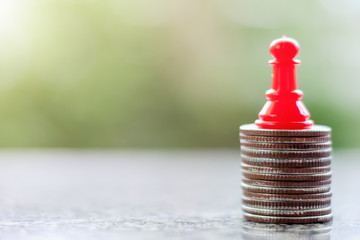 A red chess pawn on the stack of coins against blurred natural green background for investment and...