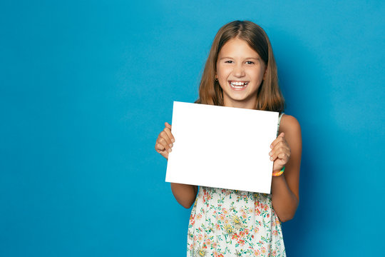 Beautiful Smiling Child (girl) With White Teeth Holding In Hands White Blank Copy Space For The Announcement