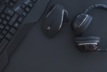 Black mouse, the keyboard, the headphones are isolated on a dark background, the top view. Flat lay gamer background. Workplace with a keyboard, mouse and headphones on a black background. Copyspace - obrazy, fototapety, plakaty