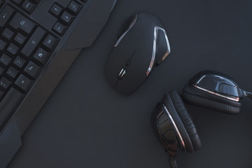 Black mouse, the keyboard, the headphones are isolated on a dark background, the top view. Flat lay gamer background. Workplace with a keyboard, mouse and headphones on a black background. Copyspace - obrazy, fototapety, plakaty