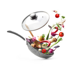 Vegetable composition. Frying pan with lid and flying vegetables, isolated on white background