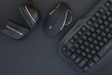 Black mouse, the keyboard, the headphones are isolated on a dark background, the top view. Flat lay gamer background. Workplace with a keyboard, mouse and headphones on a black background. Copyspace