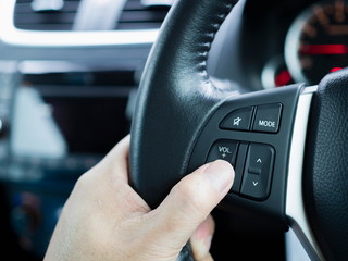 Close up driver's hands press volume button on a steering wheel