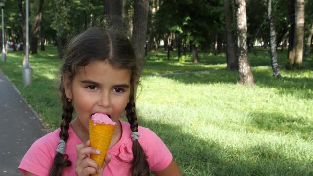 5 year old girl eating ice-cream outdoor. A beautiful, curly girl with pigtails eating ice cream in a waffle cone in the Park.