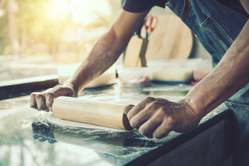 Hands chef baking dough with rolling pin on marble table