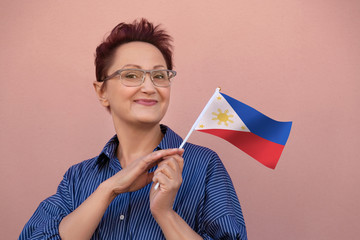 Philippines flag. Woman holding Philippine flag. Nice portrait of middle aged lady 40 50 years old with a national flag over pink wall background outdoors.