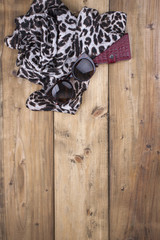 Scarf with leopard print, sunglasses and a purse made of red leather on a wooden background. Natural colors and natural ornament in fashion. Free space for text. Top view