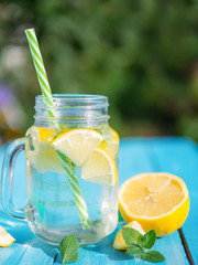 Lemonade in a glass jar with slices of lemon and mint on a wooden table