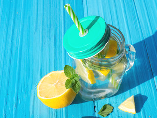 Lemonade in a glass jar with slices of lemon and mint on a wooden table