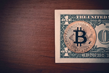 Bitcoin coin over American one dollar bill on brown wood table top