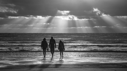 Black and white photo of three people walking at the Piha beach, west Auckland