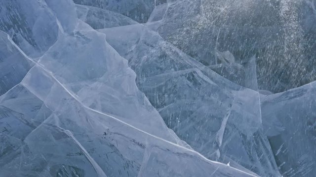 Snow is flying over surface of ice. Snowflakes fly on ice of Lake Baikal. Ice is very beautiful with unusual unique cracks. Snow sparkles and glows in red. Shooting slow motion 60fps. Picture at