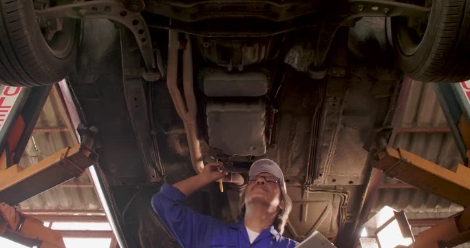 Male auto mechanic inspects the car undercarriage way in garage, car service concept. dolly shot
