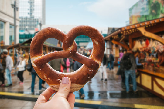 A girl or a young woman is holding a traditional German pretzel in the street. Oktoberfest festival in the background.