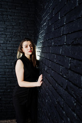 Portrait of a beautiful brunette girl in black jumpsuit in the studio next to the brick wall.