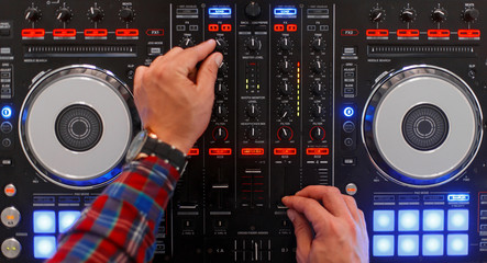 DJ in the process of work. Men's hands are played on the mixing console. Top view