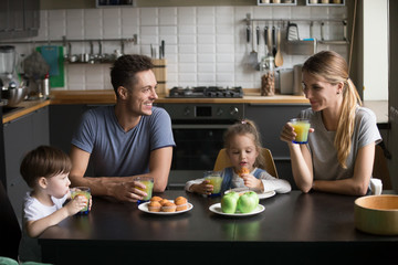 Happy family and kids having breakfast sitting at kitchen table, smiling mom and dad eating...