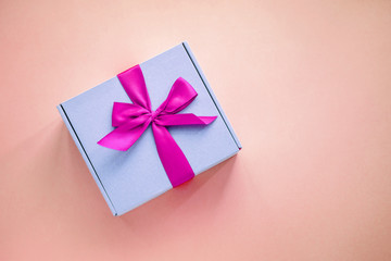 One purple paper box with bright pink ribbon bow on colored background from above. Minimalism, copy space