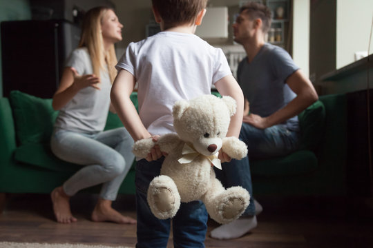 Rear view at kid boy holding toy while parents fighting, little son suffering from parents arguments, lack of attention or divorce, bad family relationships and psychological impact on child concept
