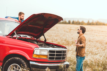 young men standing near car with broken engine in field