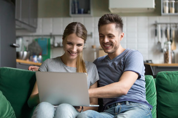 Happy millennial couple laughing looking at laptop screen together enjoying online humor, smiling...