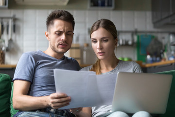 Serious confused couple checking high domestic bills with papers and laptop, millennial family...