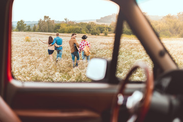 view from car at group of happy young friends walking by flower field during car trip