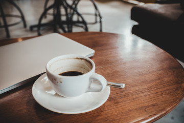 Closeup image of silver color laptop and coffee cup on wooden table with blur cafe background