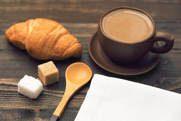 A cup of coffee, croissant and sugar cubes on a dark wooden background