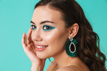 Photo closeup of stylish woman 20s wearing fashion makeup and earrings smiling and looking aside, isolated over blue background